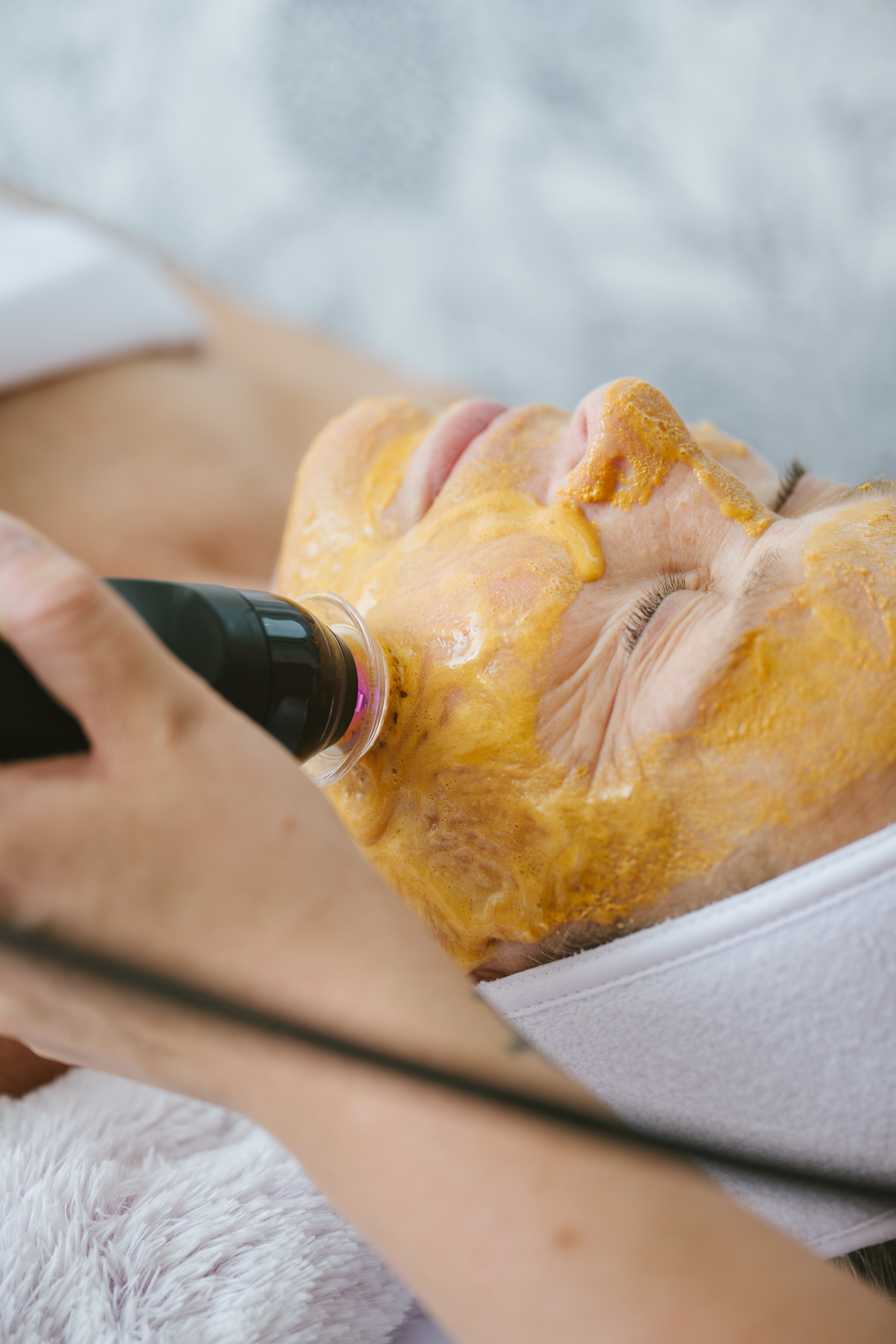 A woman undergoing a facial treatment with a golden skincare mask and a suction device for deep cleansing.