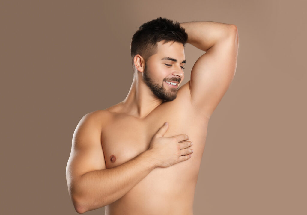 Shirtless man lifting one arm to expose the underarm against a plain studio background.