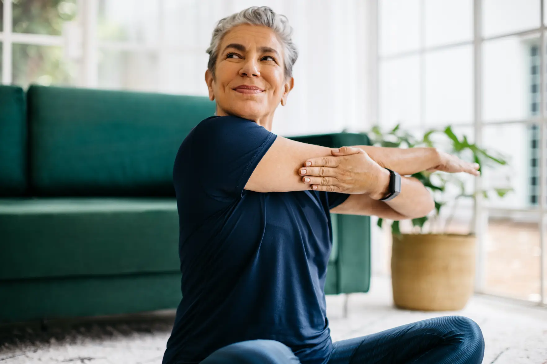Senior woman stretching arms while seated on floor in living room