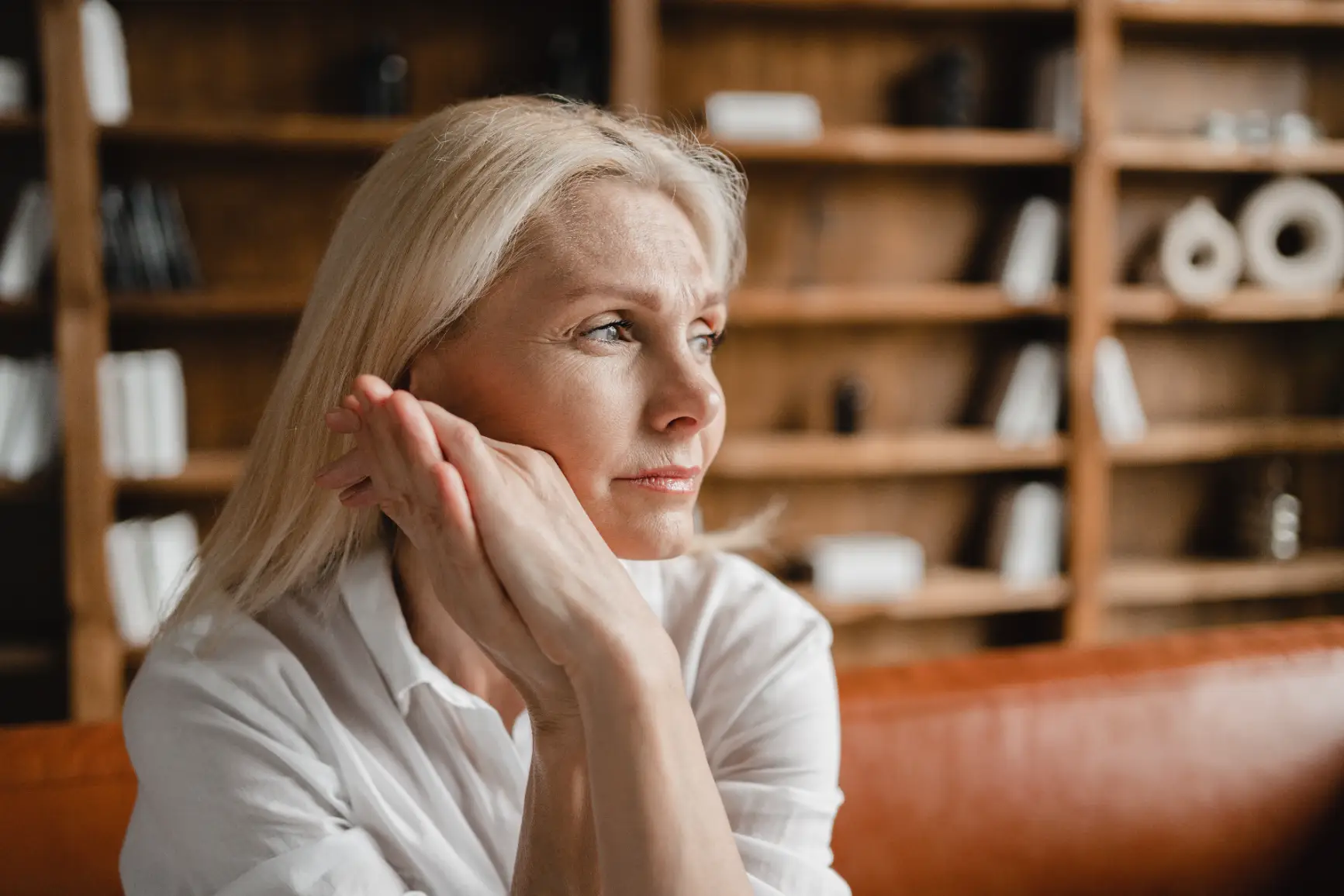 Mature woman sitting indoors with hands clasped near face