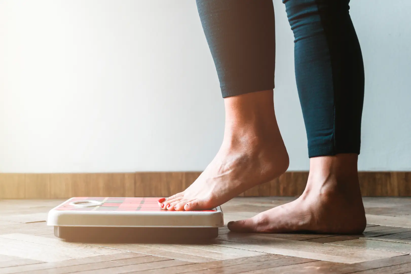 Person stepping onto a bathroom scale with one foot while standing on a wooden floor.