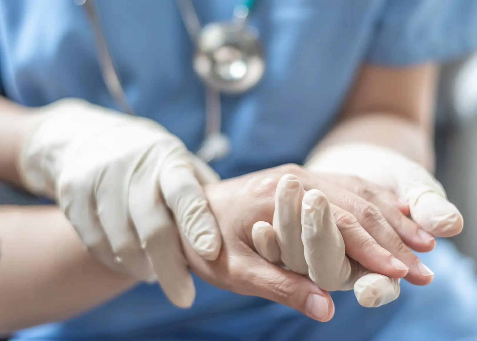 Healthcare professional wearing gloves gently examining a patient's hand during a medical assessment.