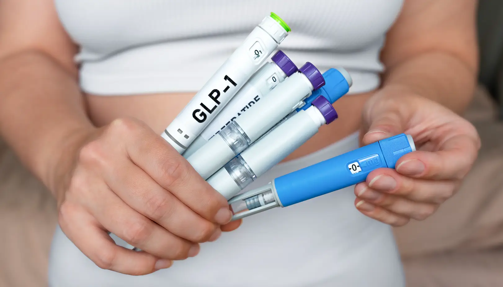 Person holding several GLP-1 injection pens in both hands against a light-colored top.