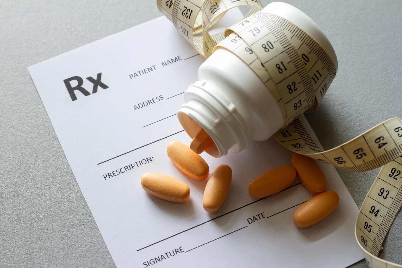 Prescription form with a pill bottle, tablets, and a measuring tape placed on top.